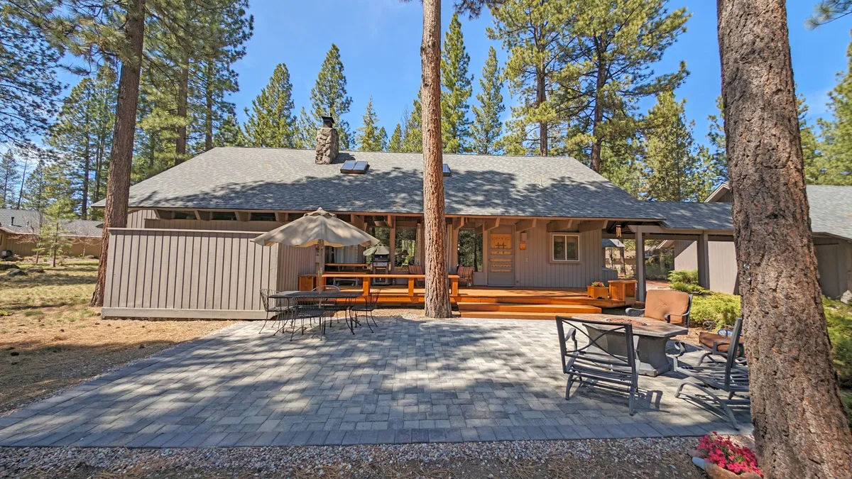 This image displays a spacious wooden deck furnished with an outdoor seating area and umbrella, surrounded by tall trees. The deck provides ample room for relaxing, dining, or allowing pets to roam while remaining close to nature.