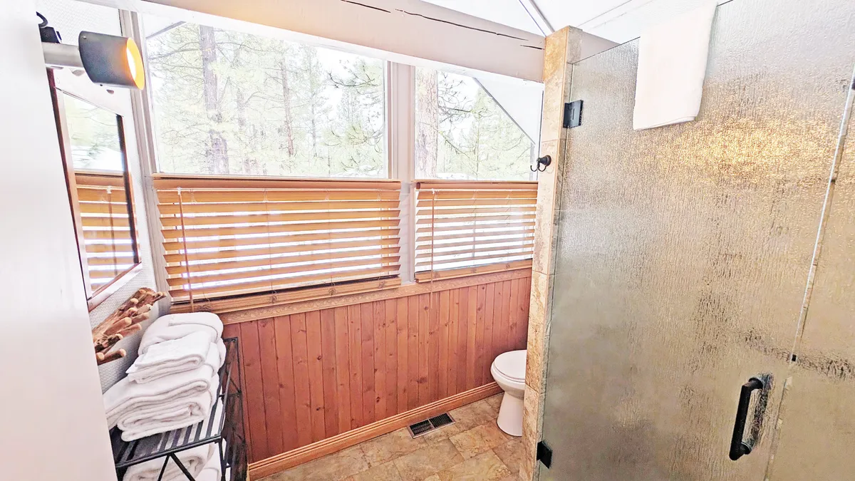 A remodeled bathroom with a glass shower, wooden paneling, towels neatly arranged, and a window with blinds. The space feels refreshed, bright, and modern, emphasizing style and convenience.