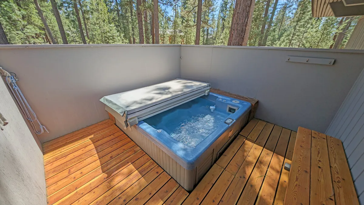 A tranquil hot tub sits on a wooden deck, surrounded by lush trees. The inviting water and scenic views suggest relaxation and stargazing, while the deck space hints at seamless indoor-outdoor living. The hot tub is the main focus, evoking a sense of privacy and indulgence.