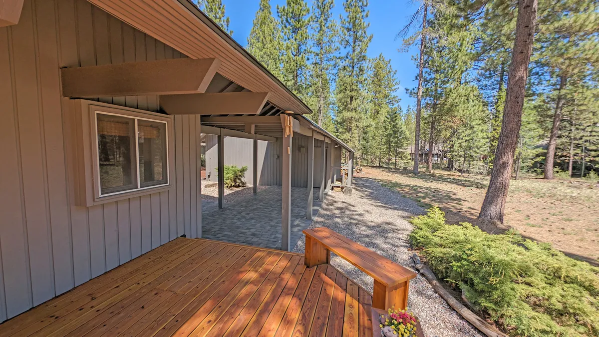 A tranquil wooden deck adorned with potted flowers, surrounded by mature trees, and leading out to a natural pathway. The open space showcases opportunities for outdoor relaxation, family gatherings, and direct access to nature trails.