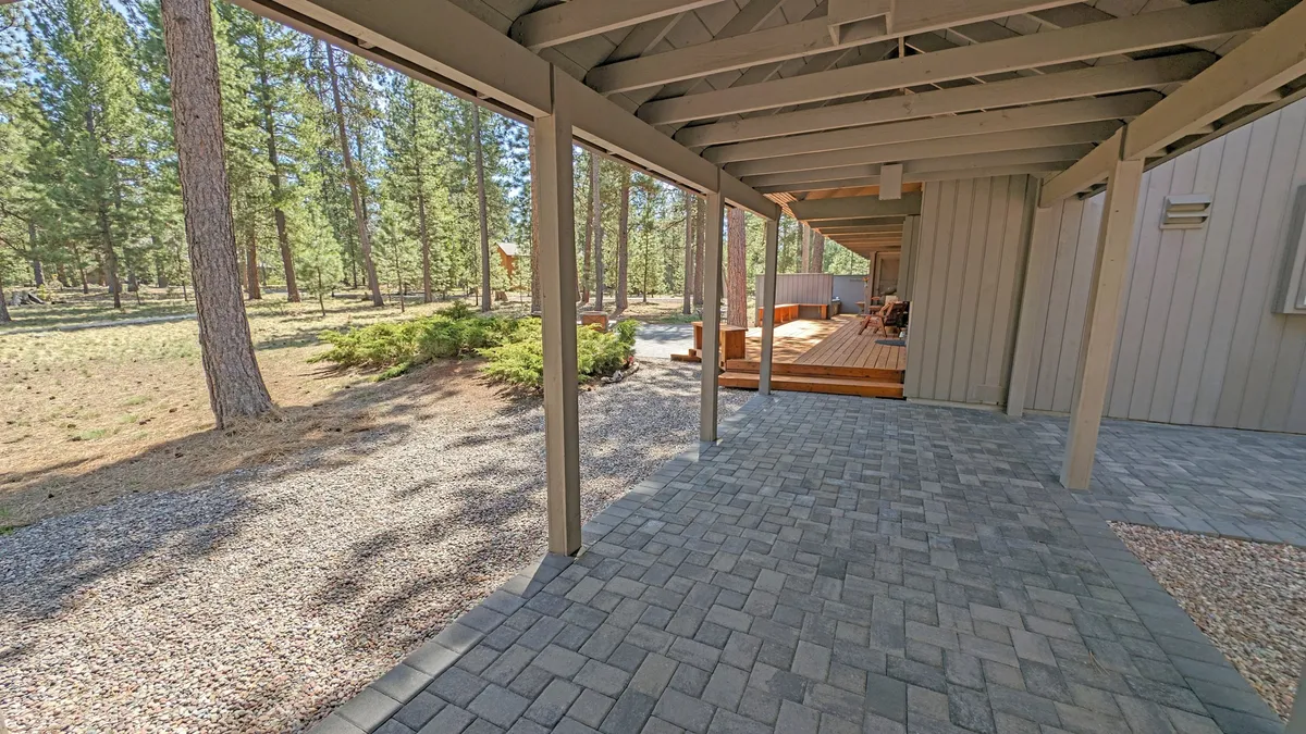 A tranquil outdoor space featuring a paved walkway, a wooden deck, and lush trees, inviting exploration and peaceful reflection. The area is ideal for morning coffee or quiet conversations surrounded by nature.