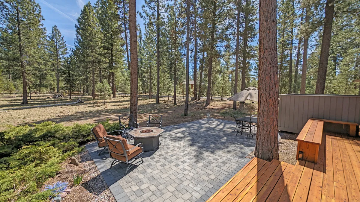 Here, a fire pit sits at the center of a patio with surrounding seating, bordered by trees and a wooden deck. It conveys opportunities for stargazing, barbecues, and communal gatherings around a fire after a day spent exploring.