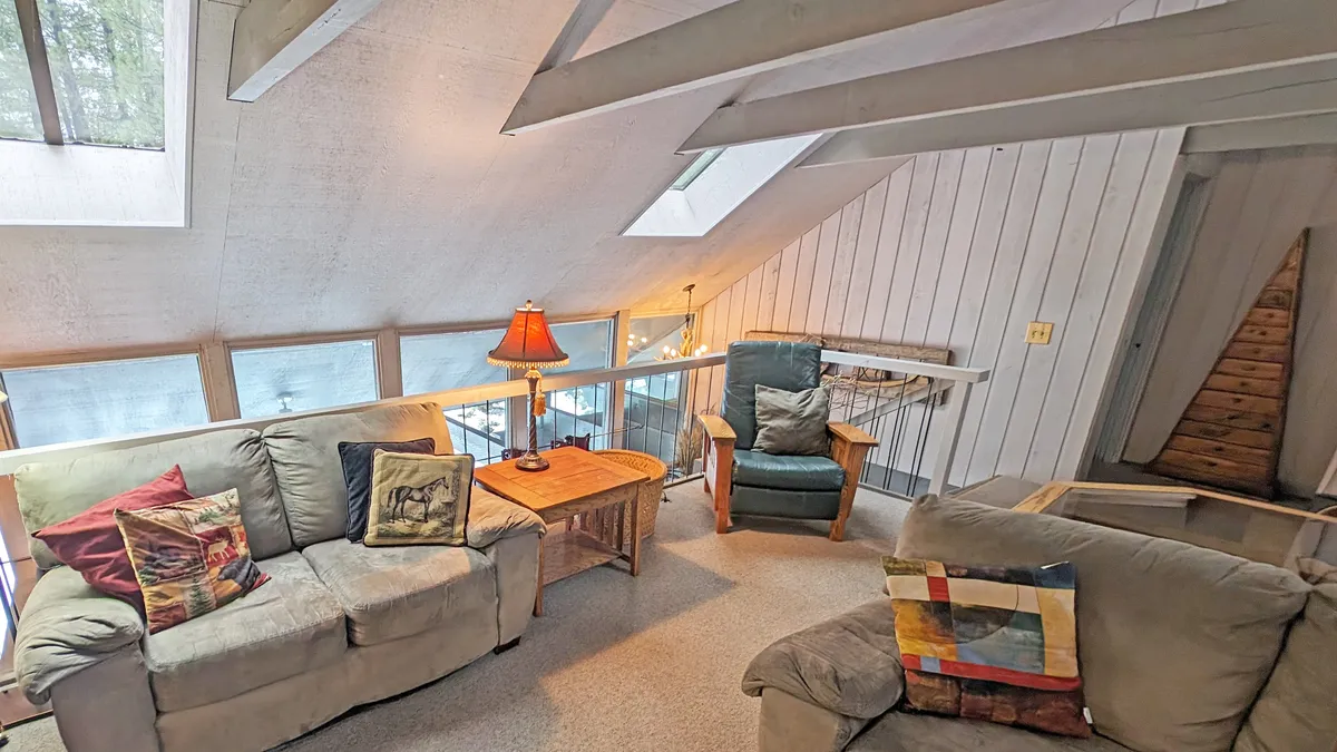 A comfortable seating area with plush sofas, a wooden coffee table, a stylish lamp, and a wooden staircase leading upstairs. Skylights add brightness, and the room feels inviting and homely—perfect for unwinding or gathering with others.