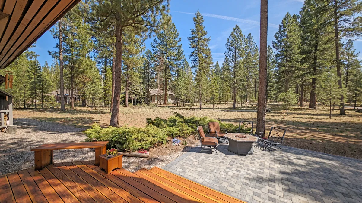 A wide wooden deck with outdoor seating and a fire pit, enveloped by trees and lush open space. The fire pit and ample seating set the stage for pet-friendly fun, campfire gatherings, and relaxed evenings. The open view of the surrounding common area enhances the sense of sanctuary.