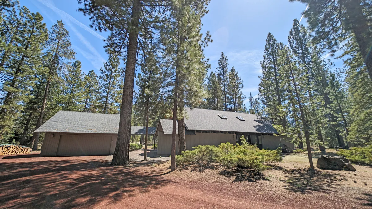 A peaceful exterior view of the house nestled among tall trees, with a driveway and an inviting front entrance. The setting evokes privacy, tranquility, and easy access to the surrounding outdoors—perfect for pet-friendly adventures.