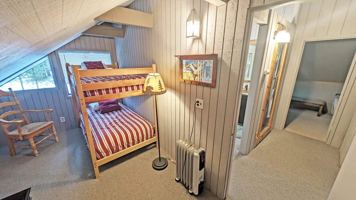A warm, inviting bedroom with a bunk bed, rocking chair, and decorative lamp. The room's layout and decor suggest a playful yet comforting atmosphere, ideal for children or groups seeking a sense of belonging.